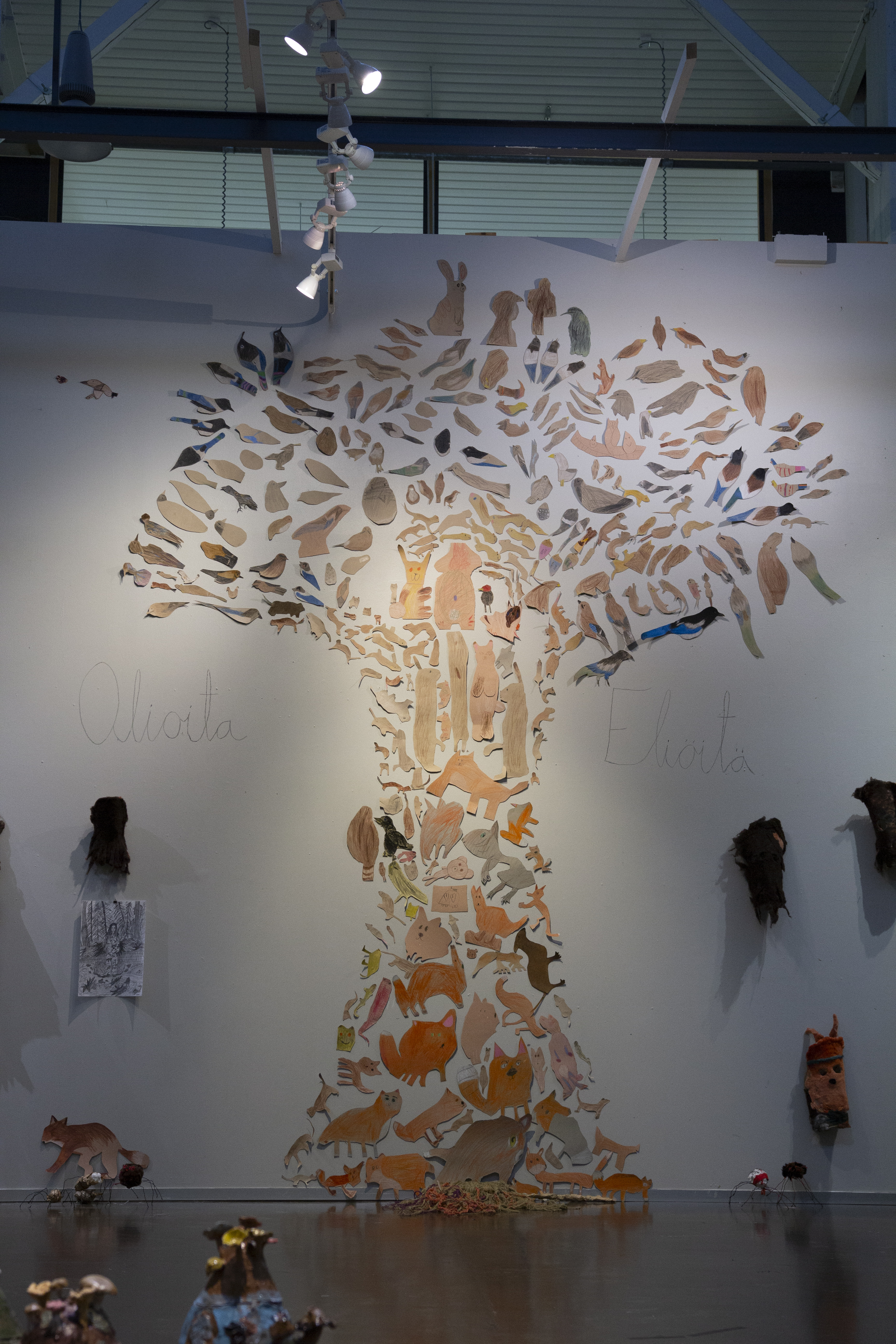 Suuri valkoiselle seinälle aseteltu puun muotoinen kollaasi, joka muodostuu muotoon leikatuista eläin- ja lintupiirroksista