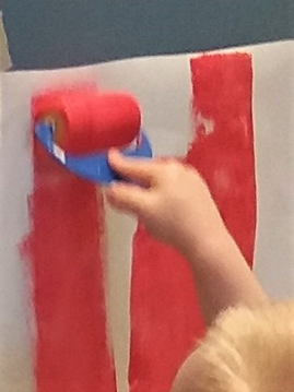 kuvassa lapsi maalaa telalla punaisella maalilla