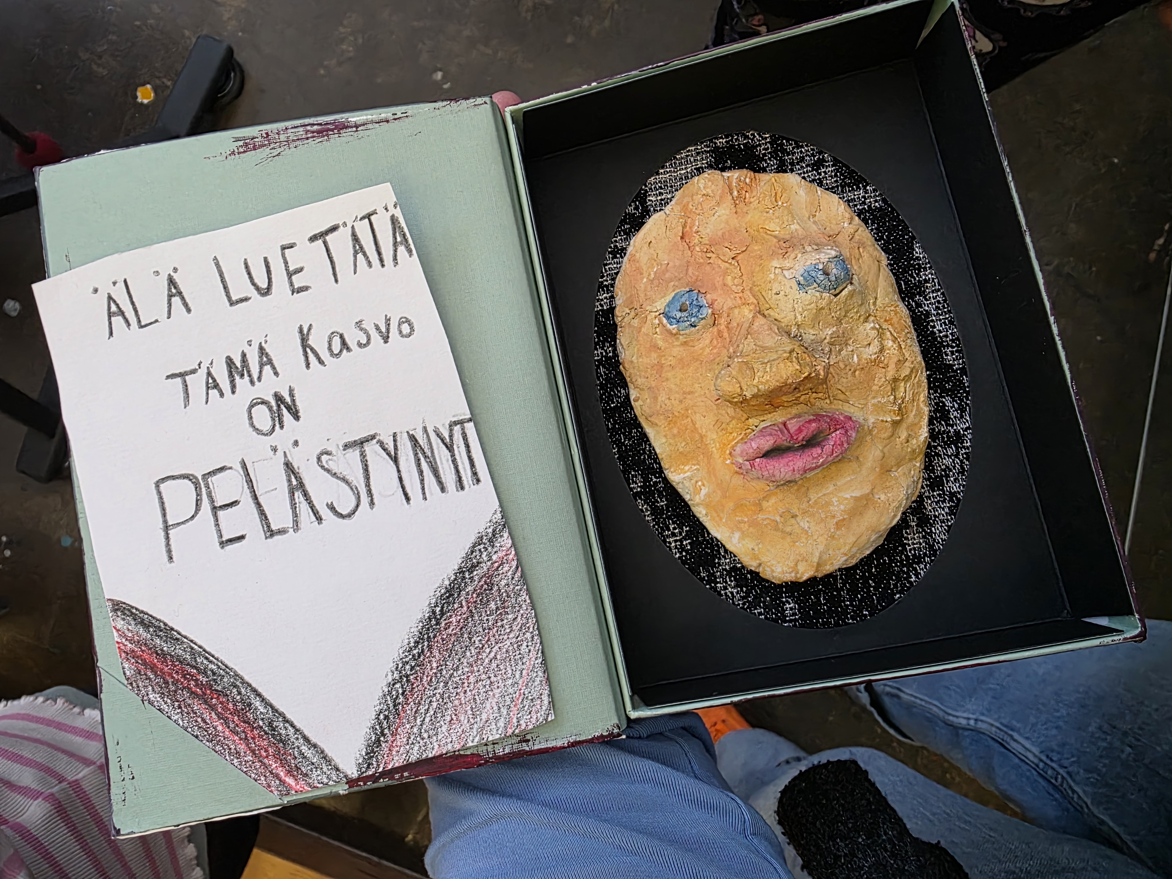 Laatikossa keramiikkakasvot, vieressä lukee: Älä lue tätä, tämä kasvo on pelästynyt