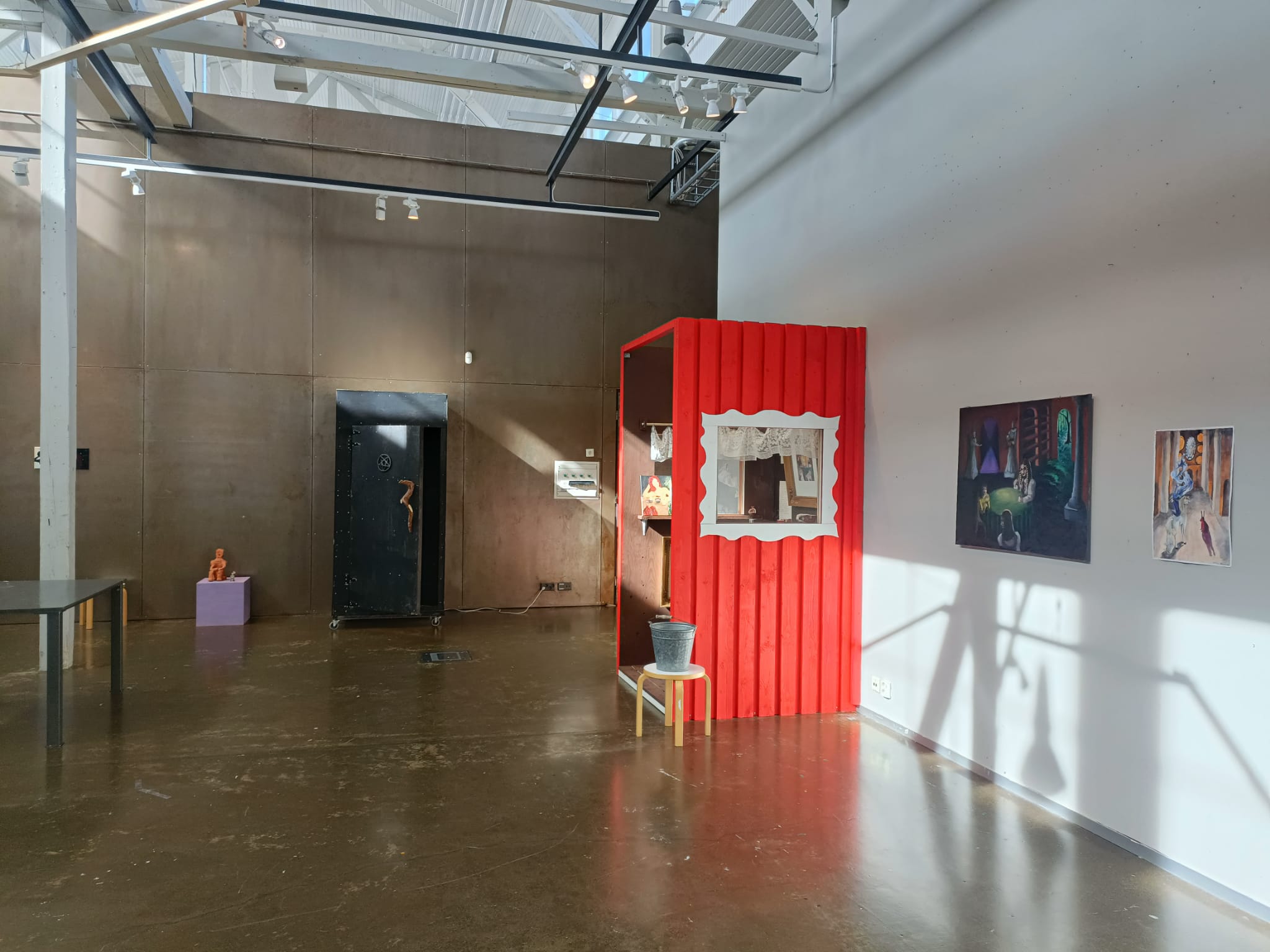 galleriatila, jossa näkyy musta huussi sekä punainen mökkimäinen rakennelma