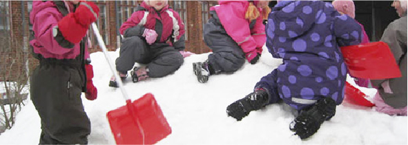 Kuusi oppilasta leikkii lumikasan päällä. Yhdellä on kädessään punainen lasten lumilapio