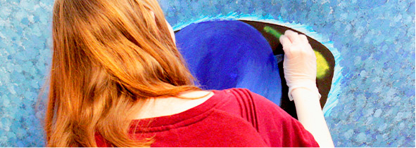 Selkäpuolelta kuvattu nuori jolla on punaiset hiukset ja punainen pusero. Tekee sinisävyistä teosta.
