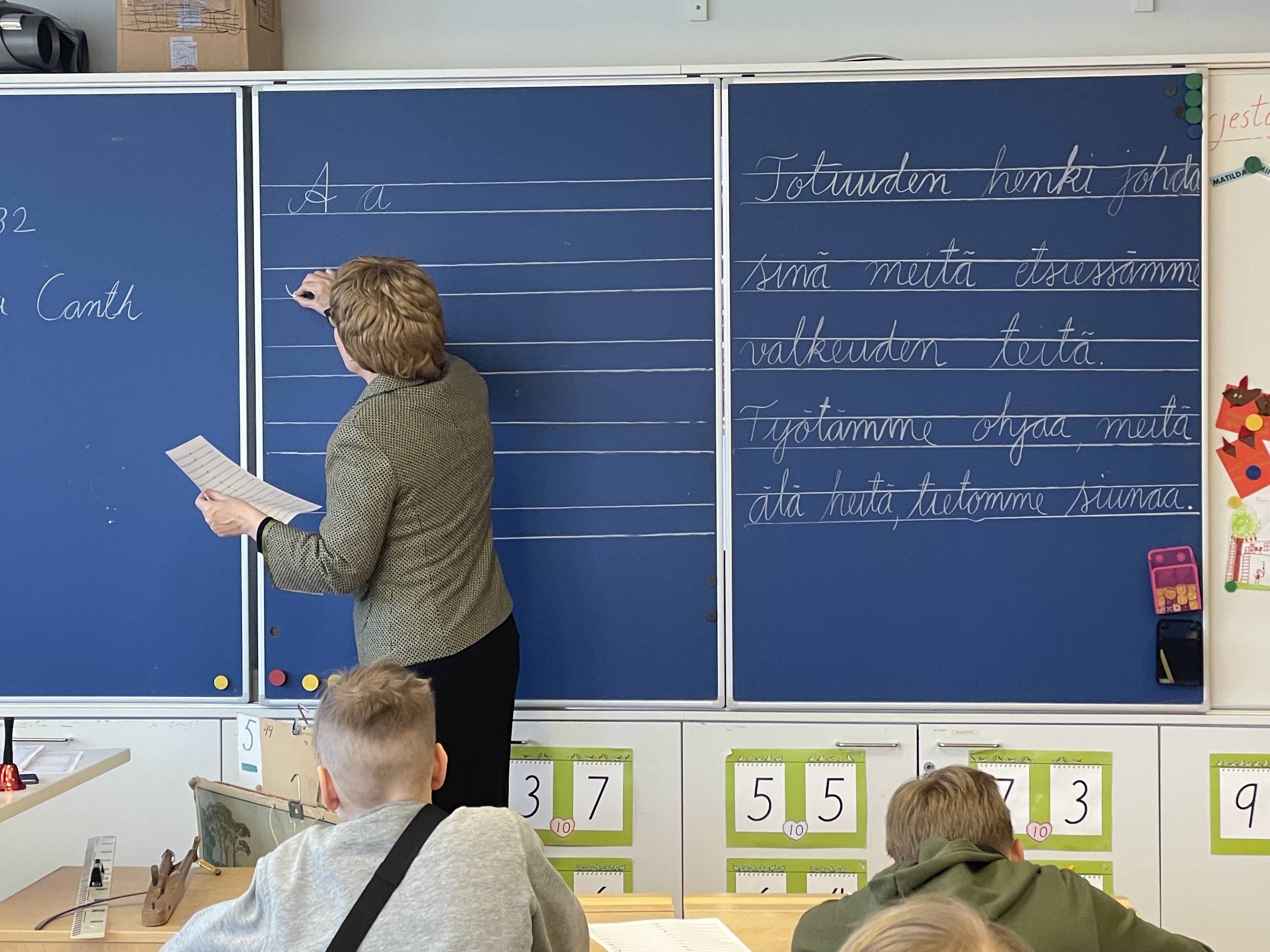 Kuvassa näkyy alakoululaisia ja vanhan ajan koulun oppitunti. 