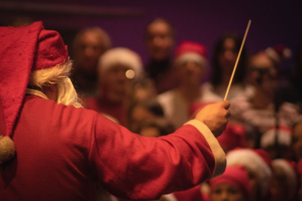 Joulupukiksi pukeutunut kapellimestari johtaa kuoroa ja orkesteria