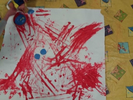kuvassa lapsen tekemä maalaus. Työ on tehty kastamalla auton renkaat punaiseen maaliin ja sen jälkeen lapsi on ajanut autolla paperin päällä, punaiset auton renkaiden jäljet näkyvät paperissa
