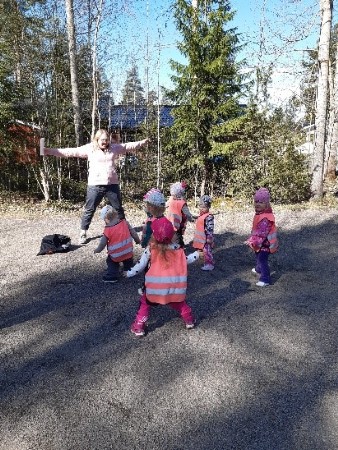 Kuvassa lapset jumppaavat ulkona hiekkakentällä oranssit turvaliivit päällä