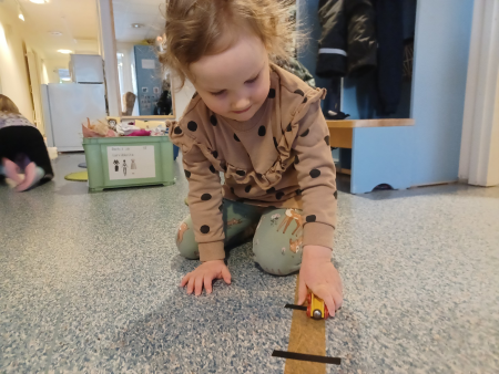 kuvassa tyttö leikkii junaradalla kädessään puinen pieni junan vaunu.