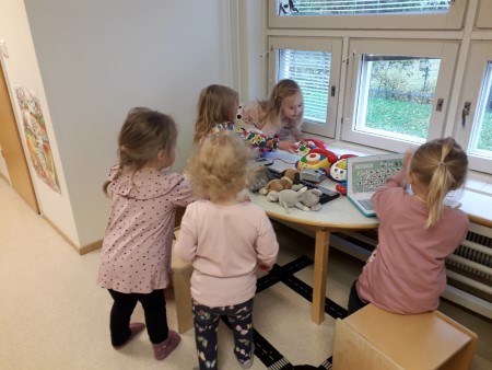viisi tyttöä leikkii toimistoleikkiä kaarevan  lastenpöydän ympärillä ryhmätilassa