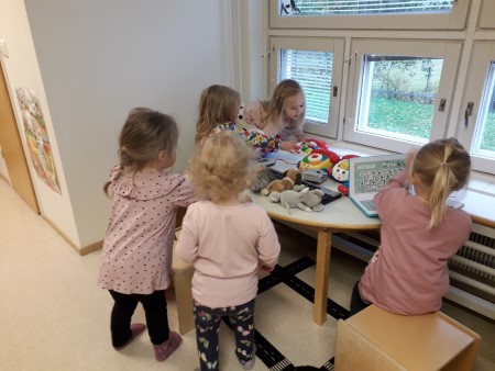 viisi tyttöä leikkii toimistoleikkiä kaarevan lastenpöydän ympärillä ryhmätilassa