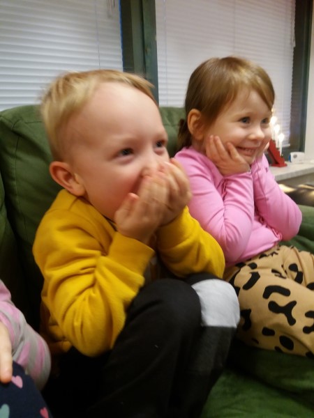 poika ja tyttö istuvat sohvalla hymyillen ja kuuntelevat tontun lähettämää kirjettä
