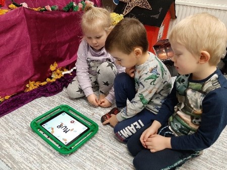kolme lasta tutkii lattialla istuen tablettia
