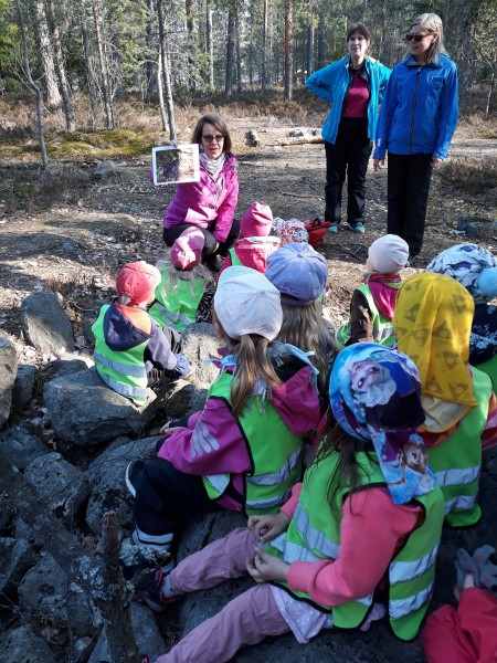 Aikuinen lukee lapsille satua metsässä